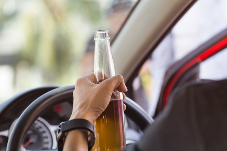 A person holding a bottle of beer while sitting behind the wheel of a car